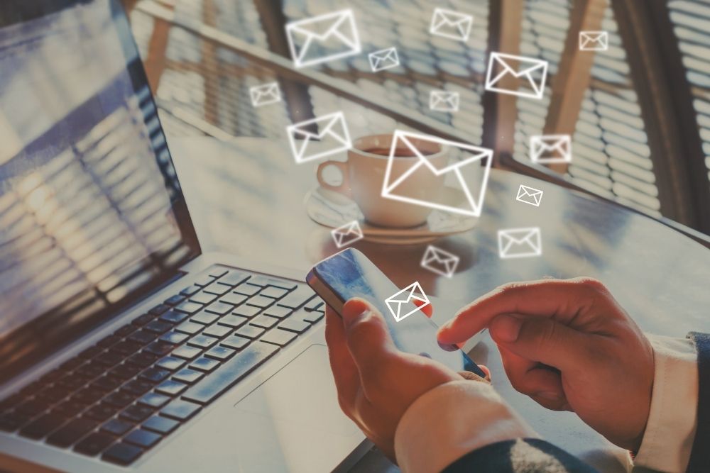 Hand of a man using a phone and laptop with email icons floating