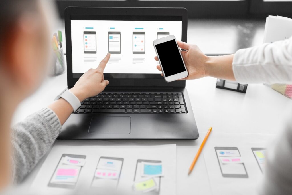 Two people collaborating on responsive web design, reviewing layouts on laptop and phone.