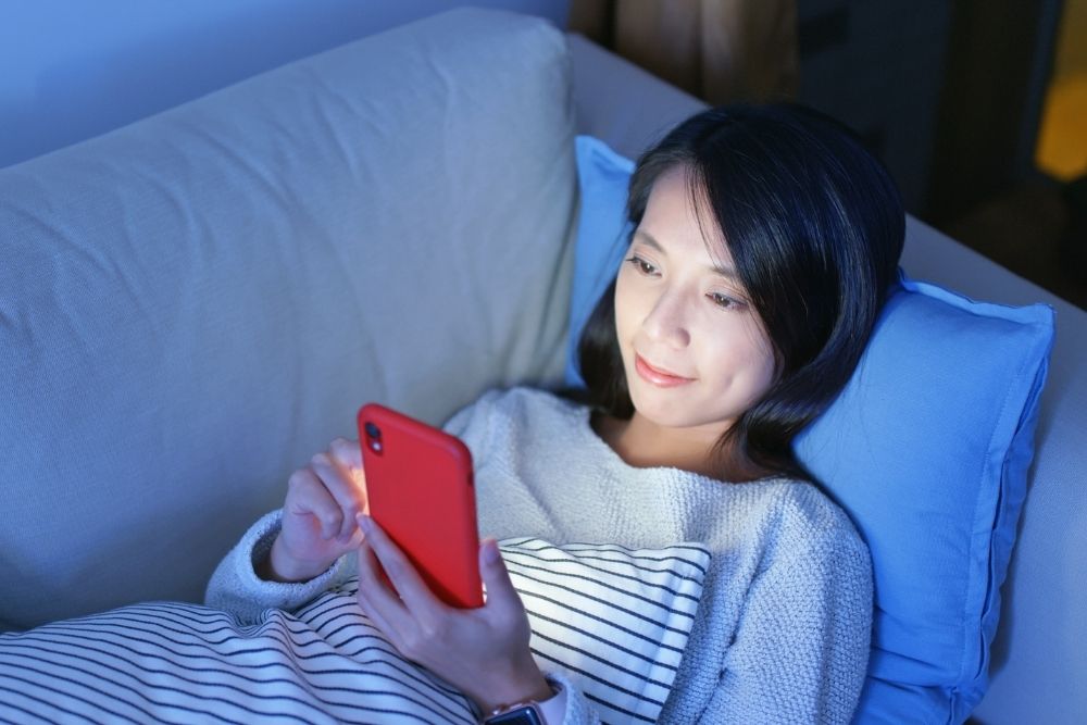 Woman checking evening customer messages on her phone during after-hours support.