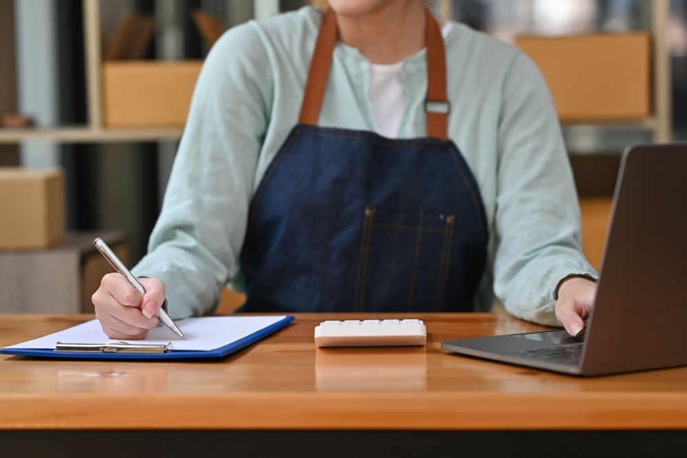 Business owner tracking and auditing their lead response time with a notebook and laptop.