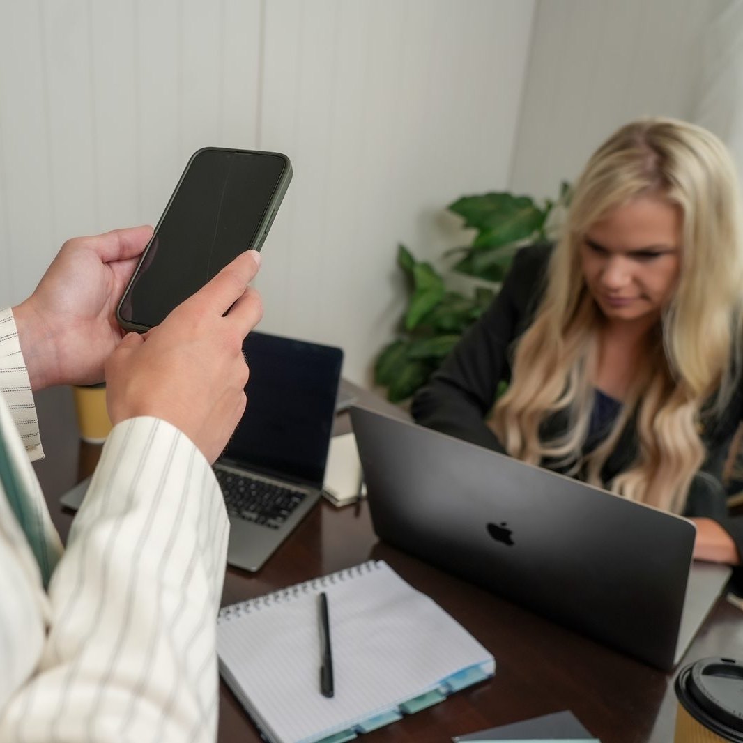 Nicole and Megan working together at a desk with laptops, a notebook, and a phone